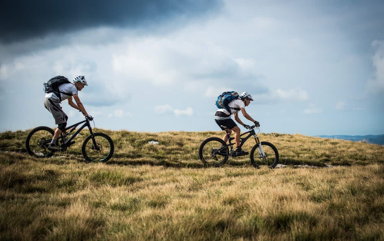 Two mountain bikers ride along a grassy trail on an overcast day.