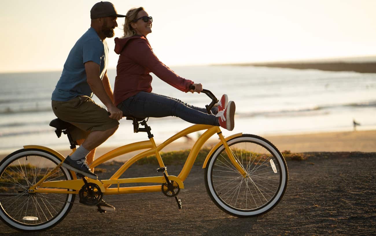 A couple ride a yellow tandem bike above a beach at sunset.