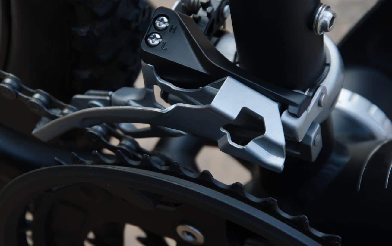 Close-up of a silver front derailleur on a matt black bike.