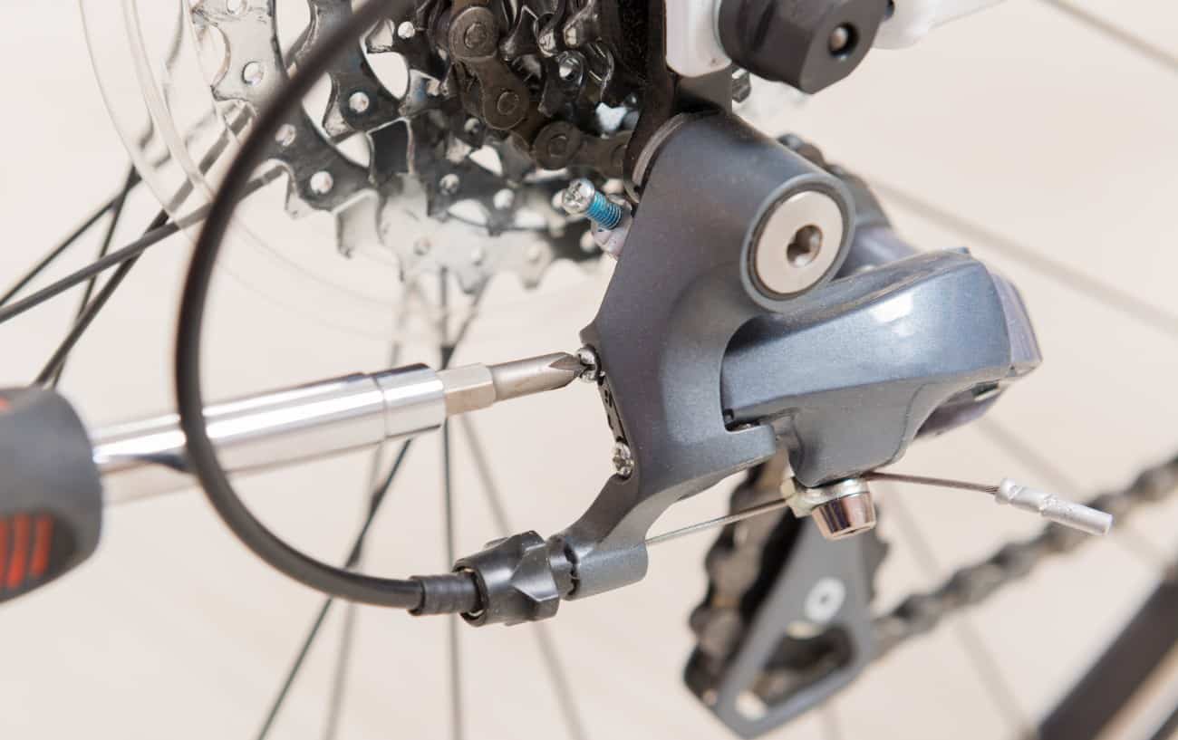 Close-up of a rear bike derailleur being adjusted with a screwdriver.