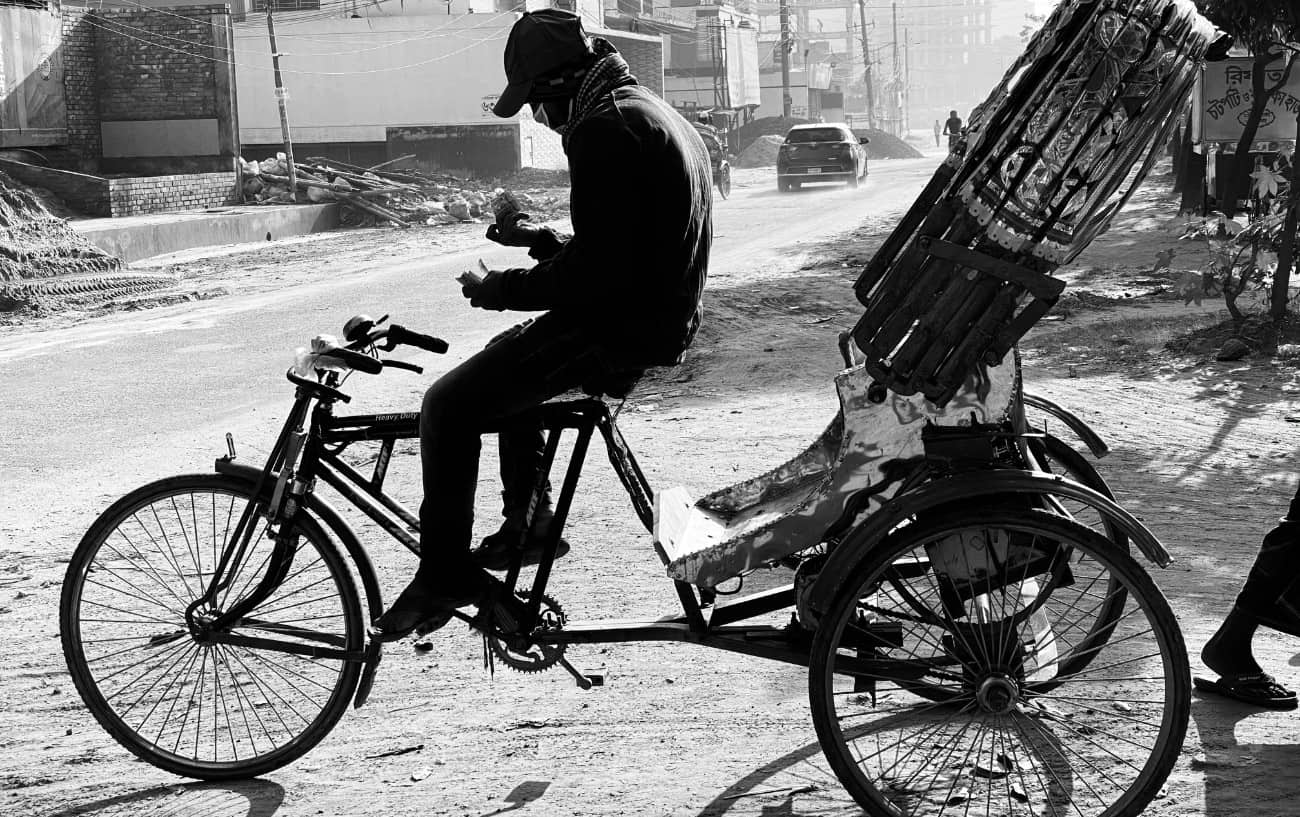 Black and white photo of a man sitting on a rickshaw tricycle.