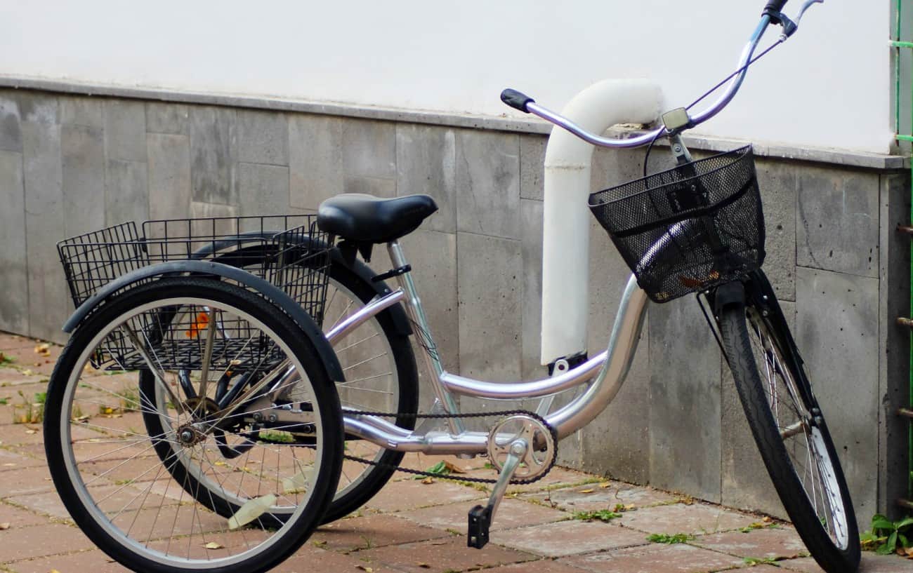 A silver adult tricycle sits on the pavement.