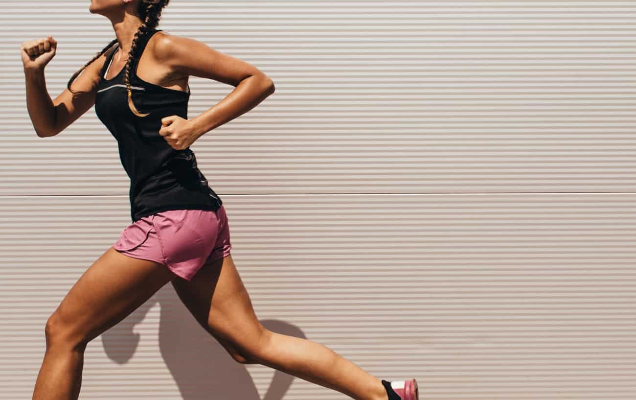 A woman in pink shorts and a black top runs beside a striped wall.