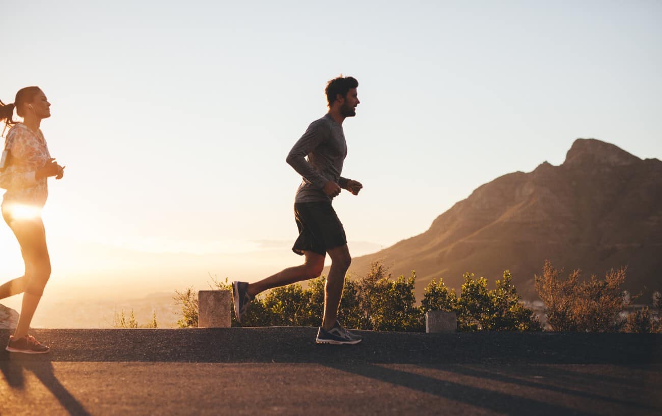 A man and a woman jog along a mountain road at sunset.