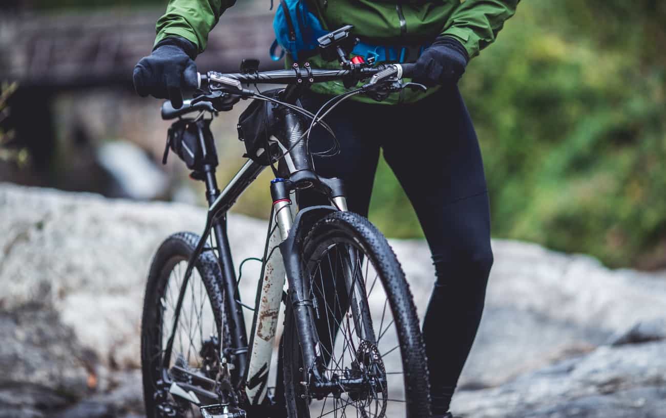Close-up of a black XC bike being wheeled across a stony landscape.