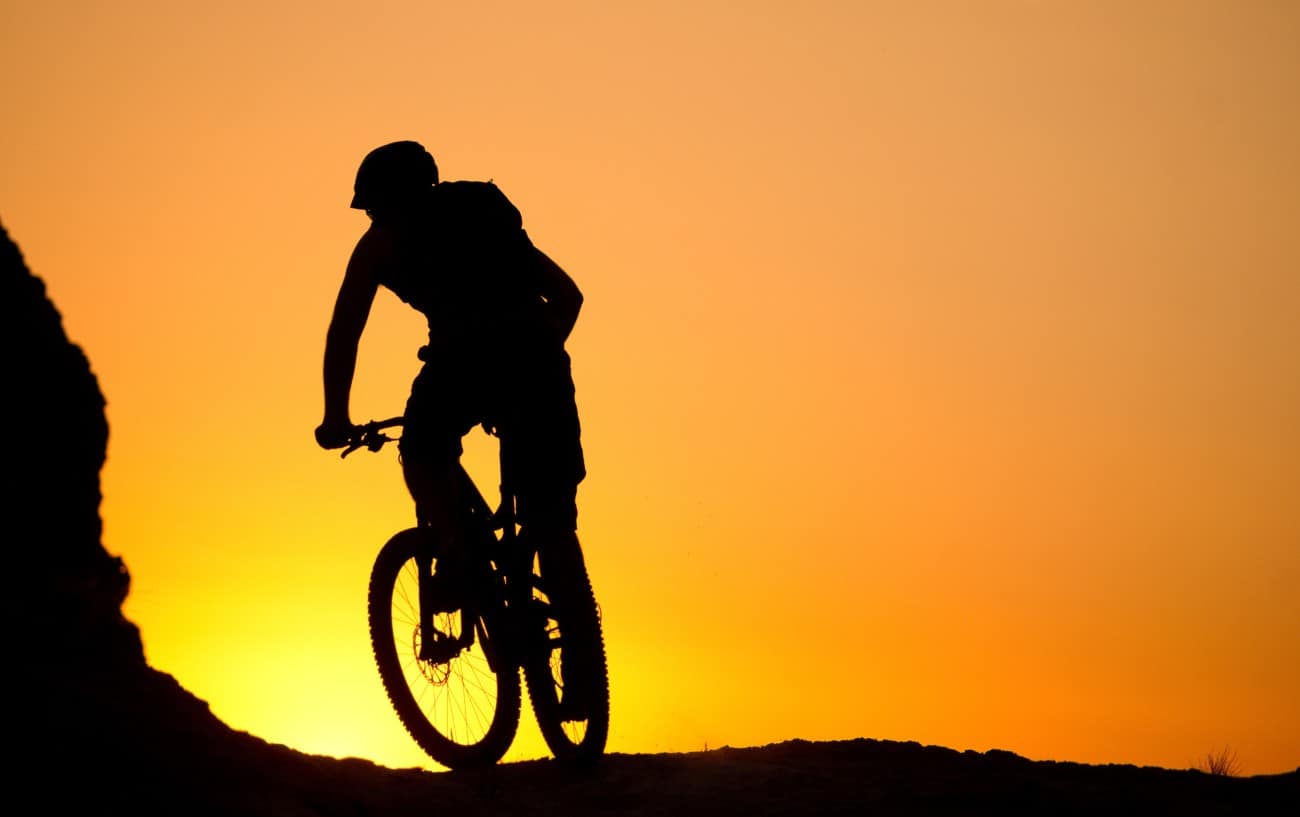 Silhouette of a cyclist on an XC mountain bike against an orange sunset.