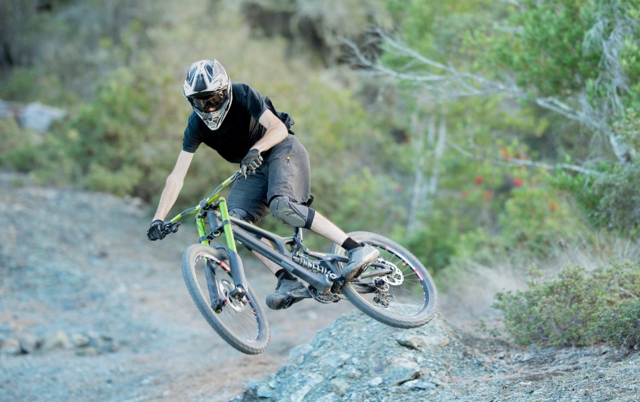 A rider pulls a stunt on a green downhill mountain bike.