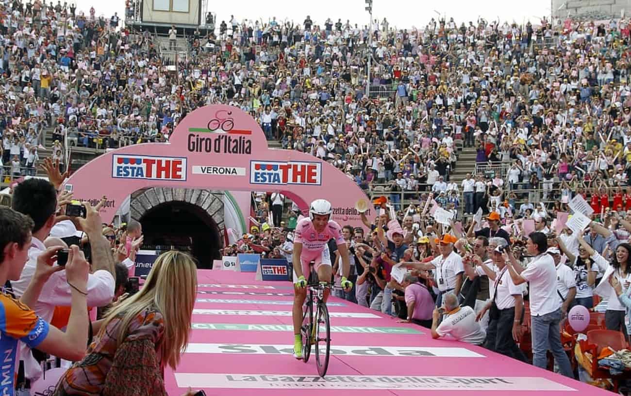 A cyclist in the maglia rosa at the Giro d'Italia - one of the cycling Grand Tours - starts a time trial in a stadium.