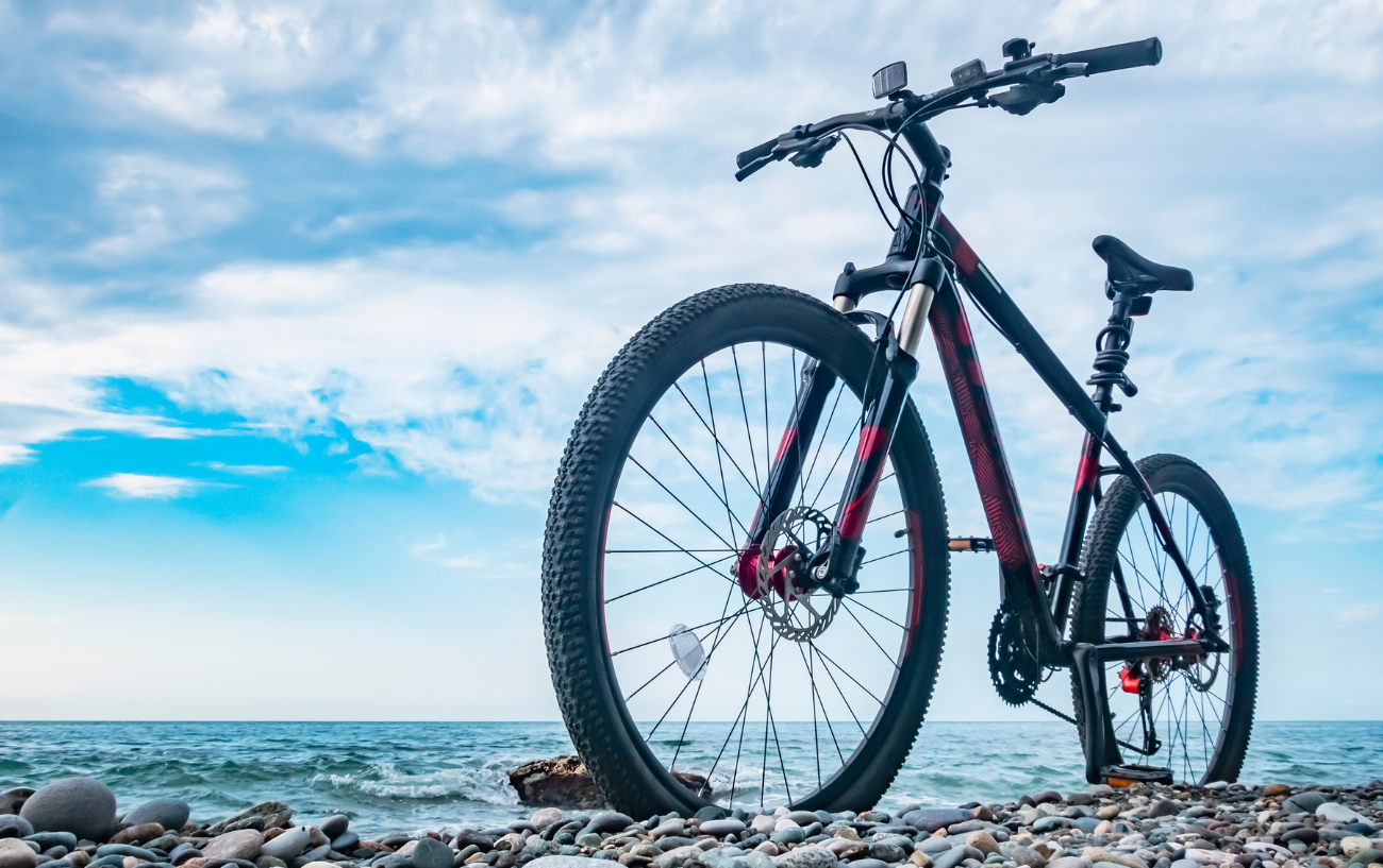 A black hardtail mountain bike sits on a pebbly beach.
