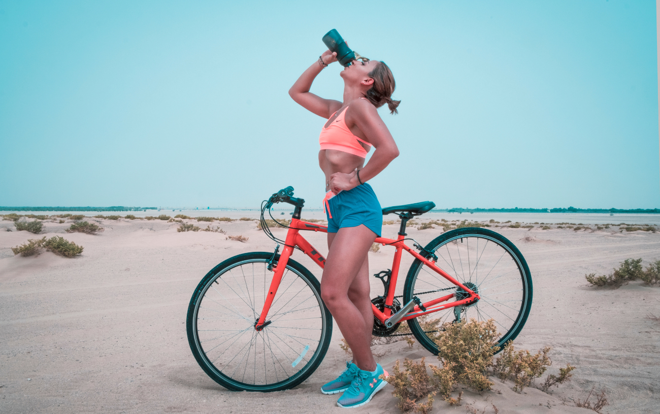 A woman stands by a red rigid mountain bike on a sandy beach.