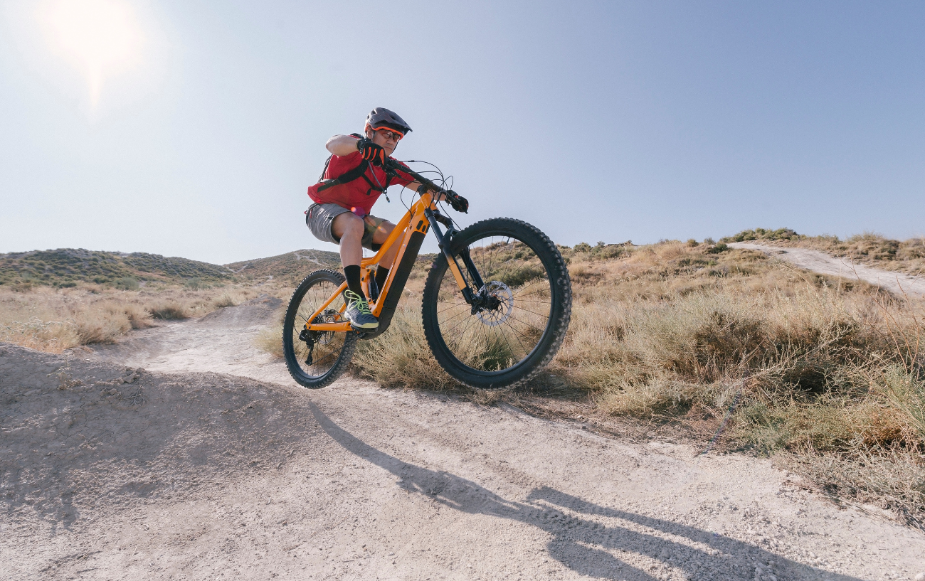 A rider jumps off a lip on an orange trail bike.