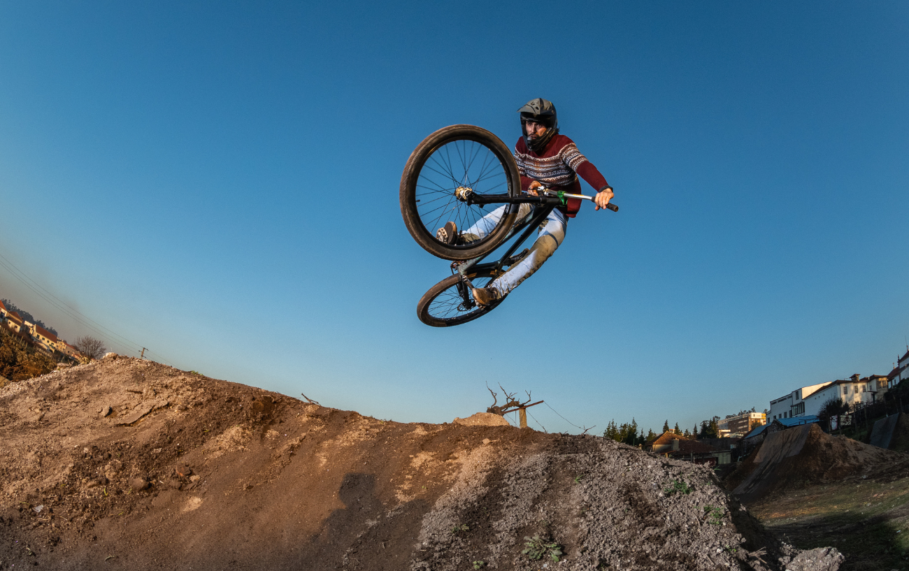 Fish-eye shot of a cyclist on a dirt jumper bike taking on a muddy trail at sunset.