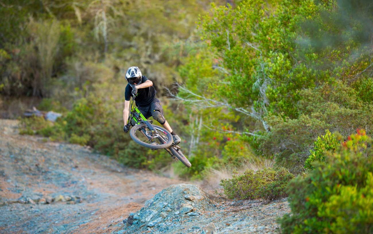 A cyclist on a green dirt jumper bike launches himself off a rocky jump.