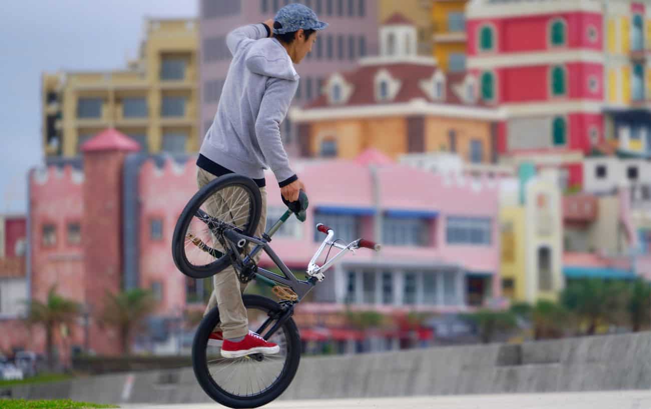 A trick rider performs nose wheelie stunts on a BMX bike.
