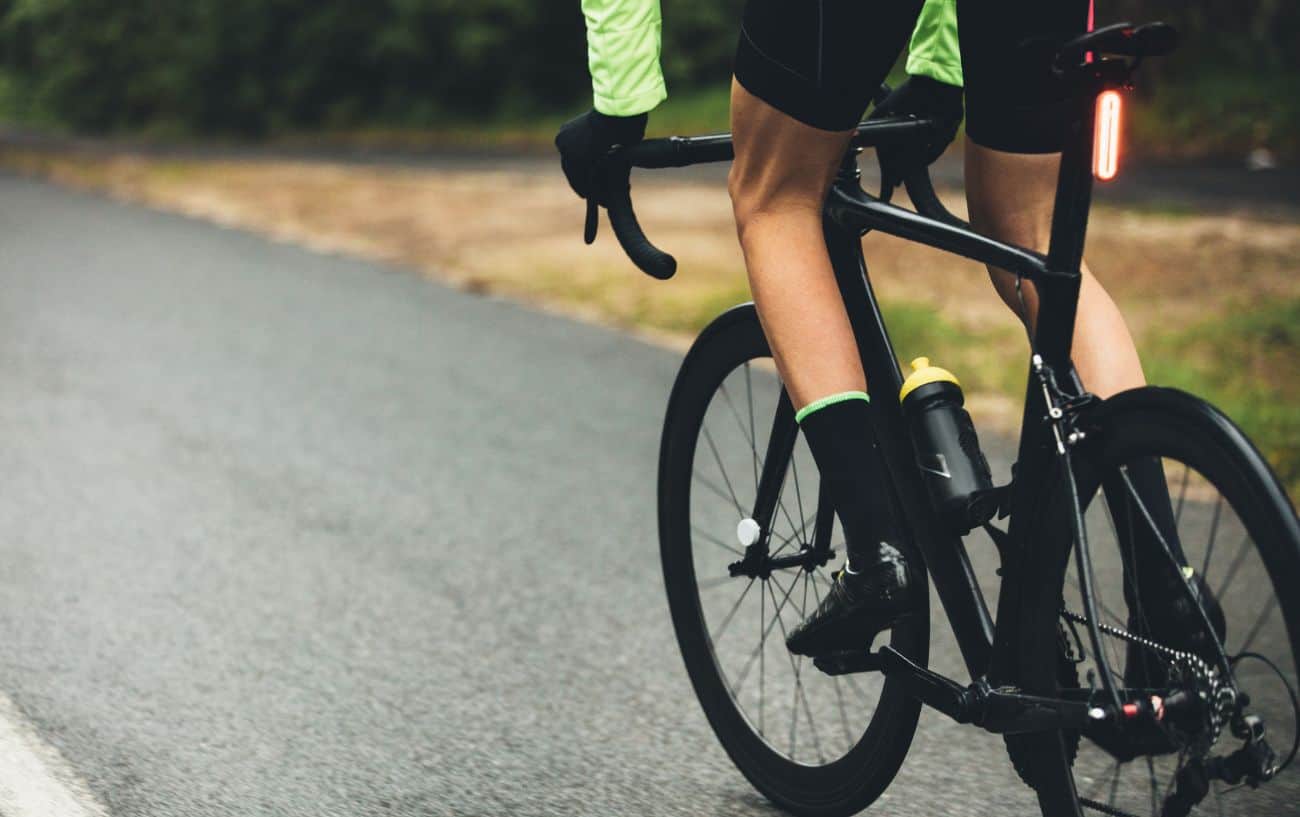 A cyclist rides a black road bike through the rain on a tarmac lane.