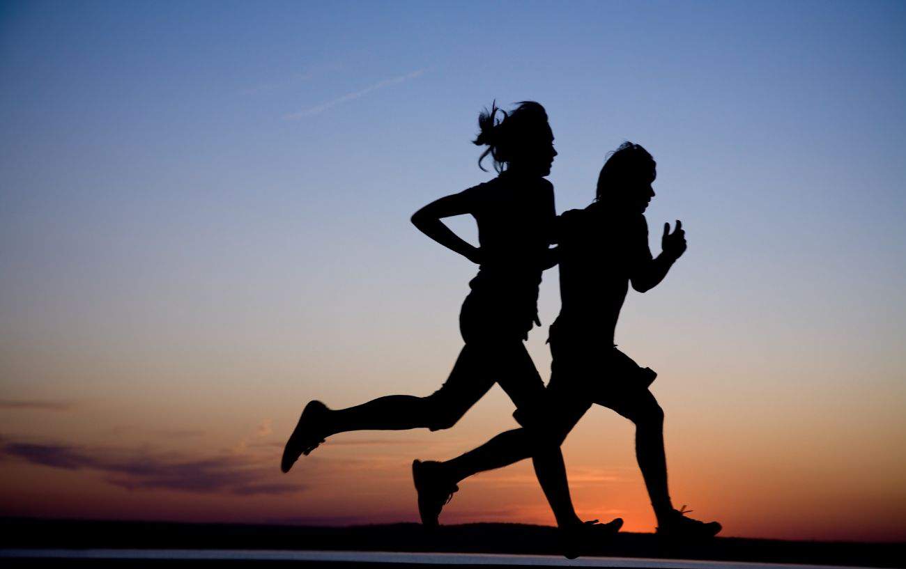 Two joggers are silhouetted against the sunset.