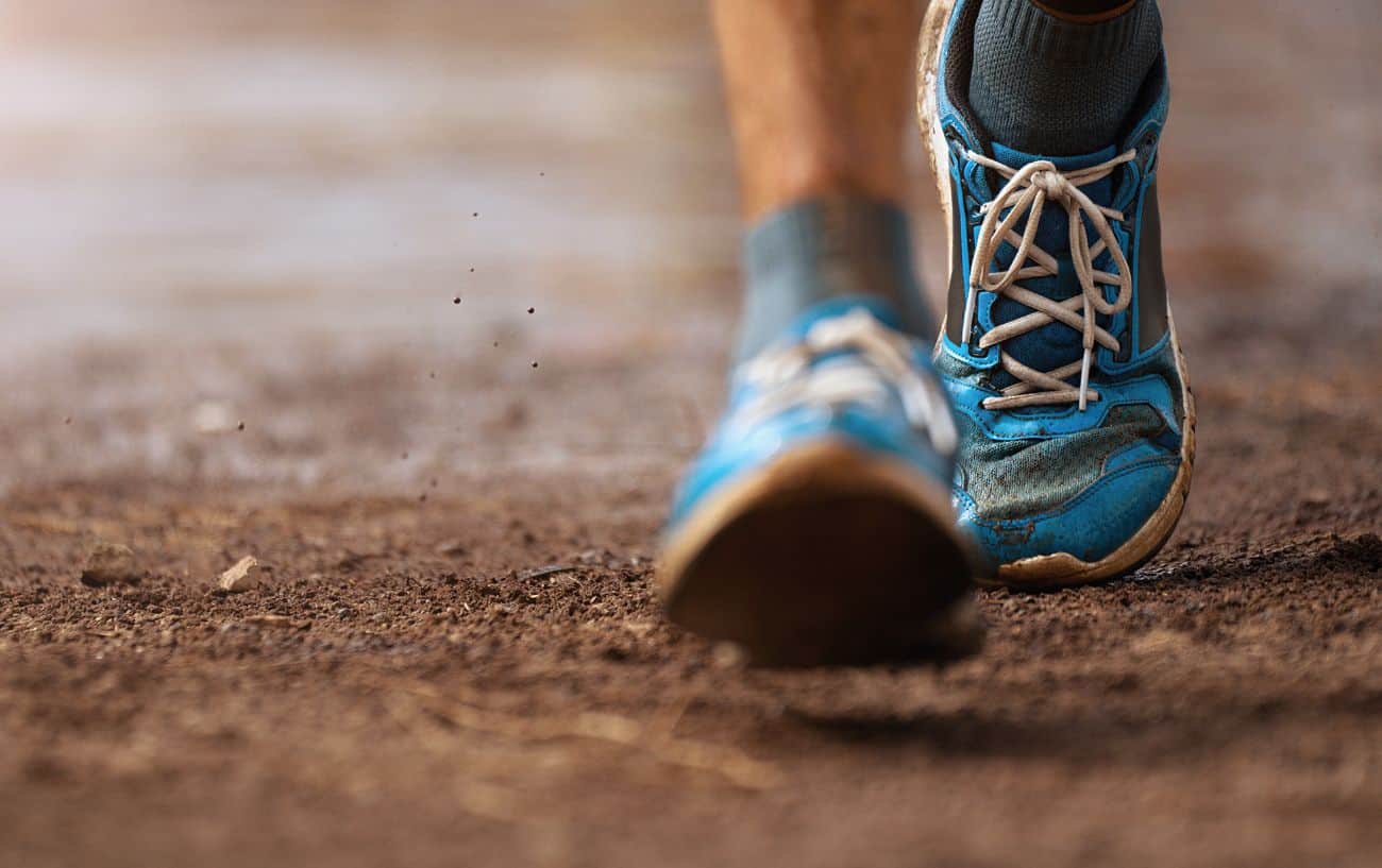 Close-up shot of someone running on a dirt track in blue running shoes.