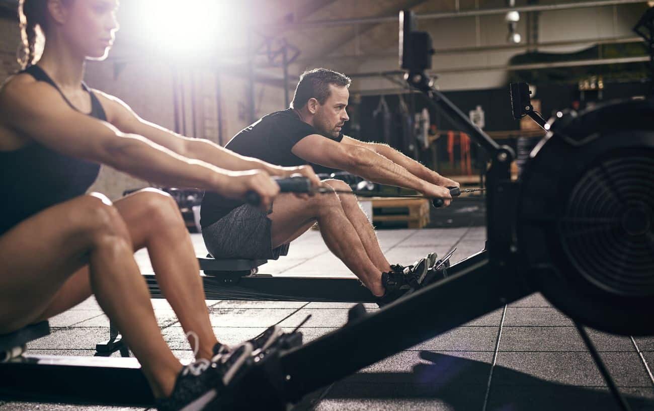 Two people cross training on rowing machines at the gym.
