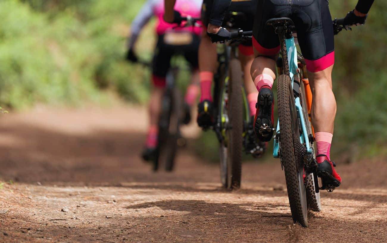 A group of cyclists on mountain bikes ride along a muddy trail.