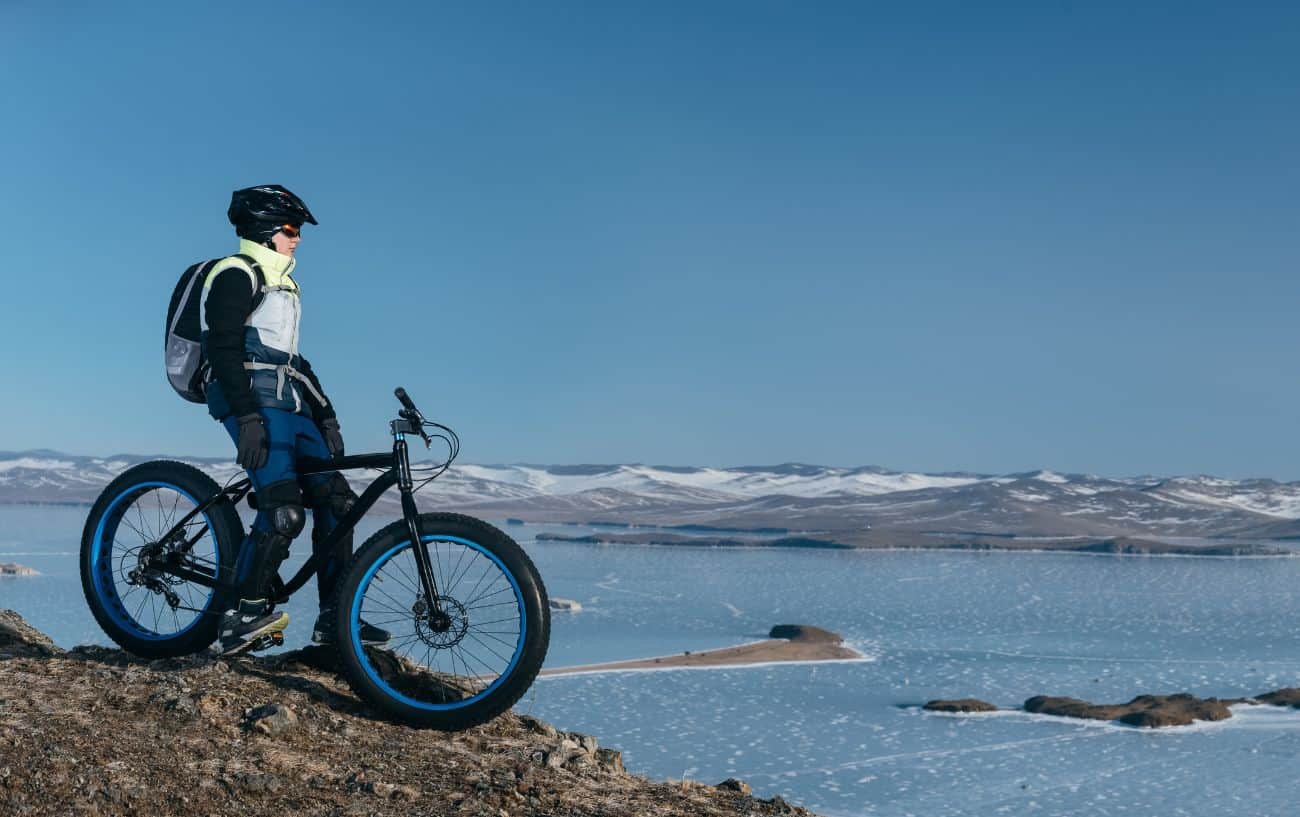 A cyclist on a fat tire bike sits atop a hill overlooking an Antarctic landscape.