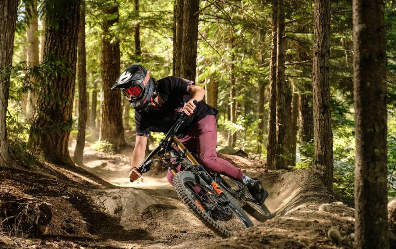 A mountain biker rounds a berm on a dirt trail through a forest.