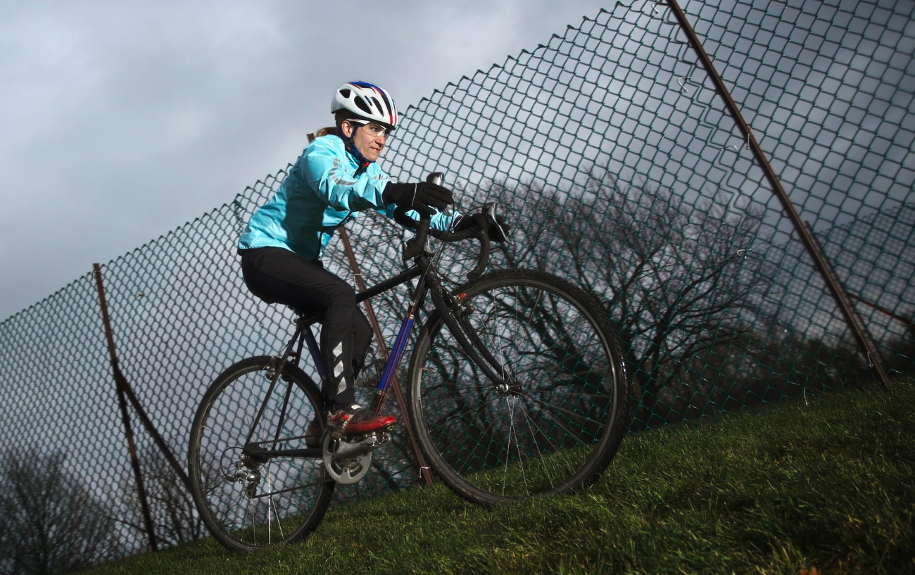 A cyclocross rider on a black bike pedals up a steep grassy slope.