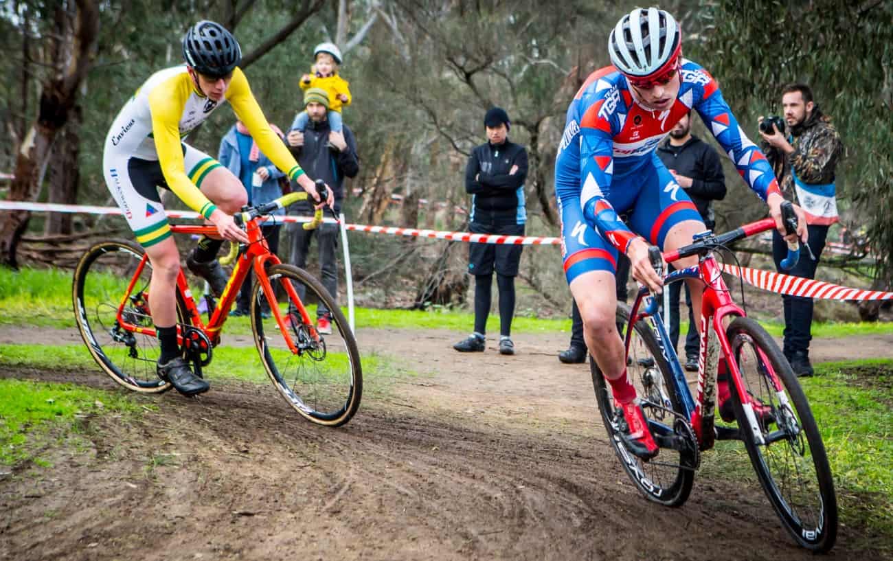 Two professionals on CX bikes compete in a cyclocross race.