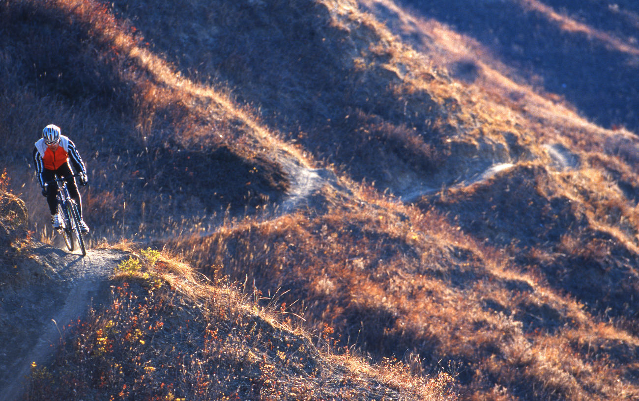 A cyclocross rider traverses a dirt track at sunset.