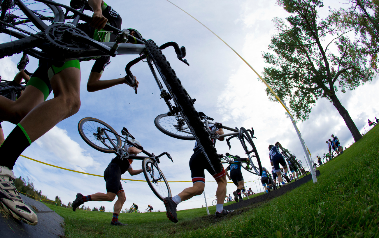 A group of cyclocross riders race to carry their bikes up a flight of stairs.