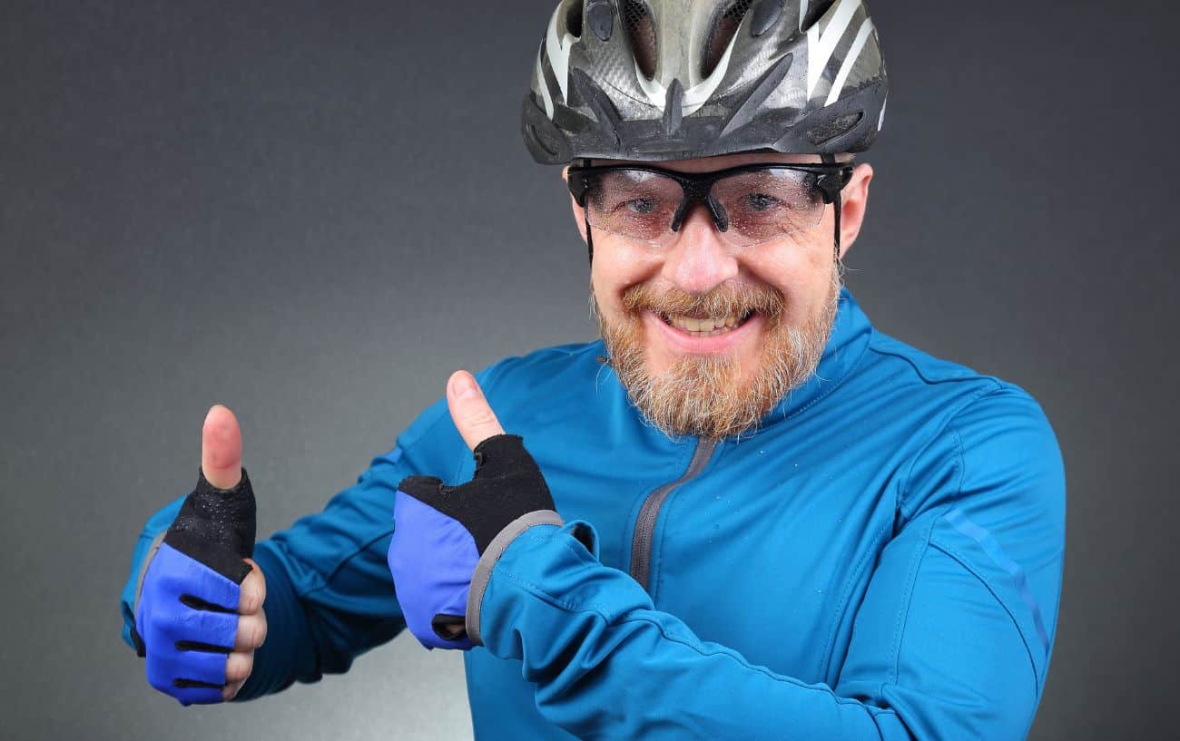 A cyclist in a blue jersey grins with both thumbs up.