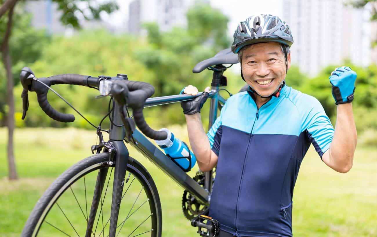 A man grins and pumps his fist while carrying a grey road bike.