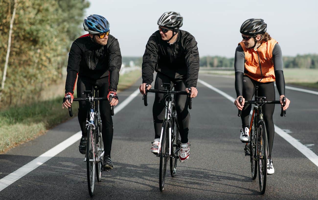 Three cyclists ride alongside each other on a paved road.
