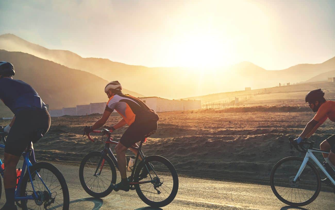 A group of cyclists ride through a valley sunset.
