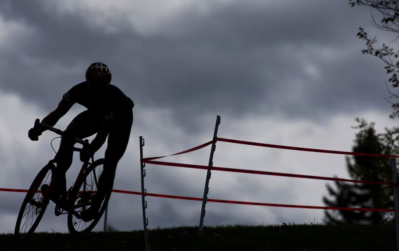 A cyclocross rider is silhouetted as they come around a corner.