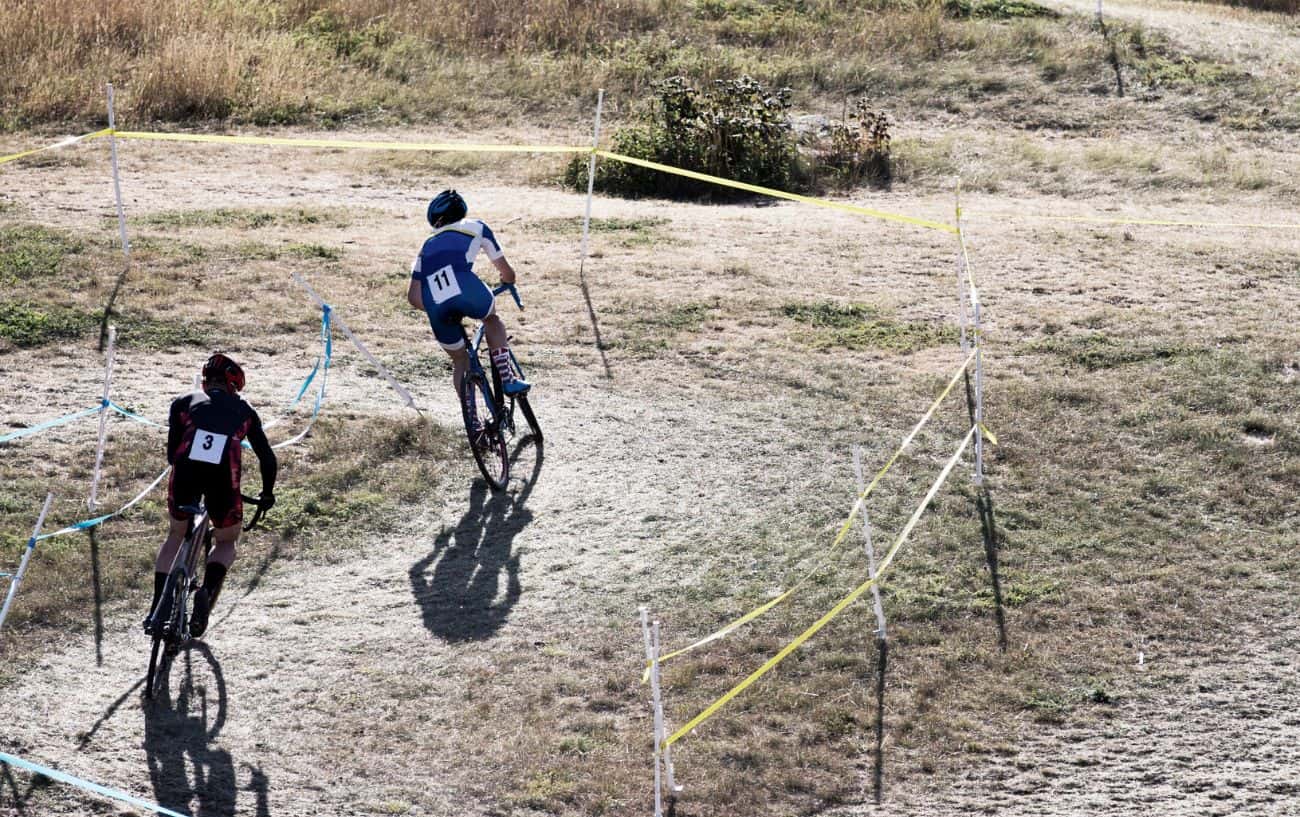 Two cyclocross riders navigate twisty turns on a grassy course.