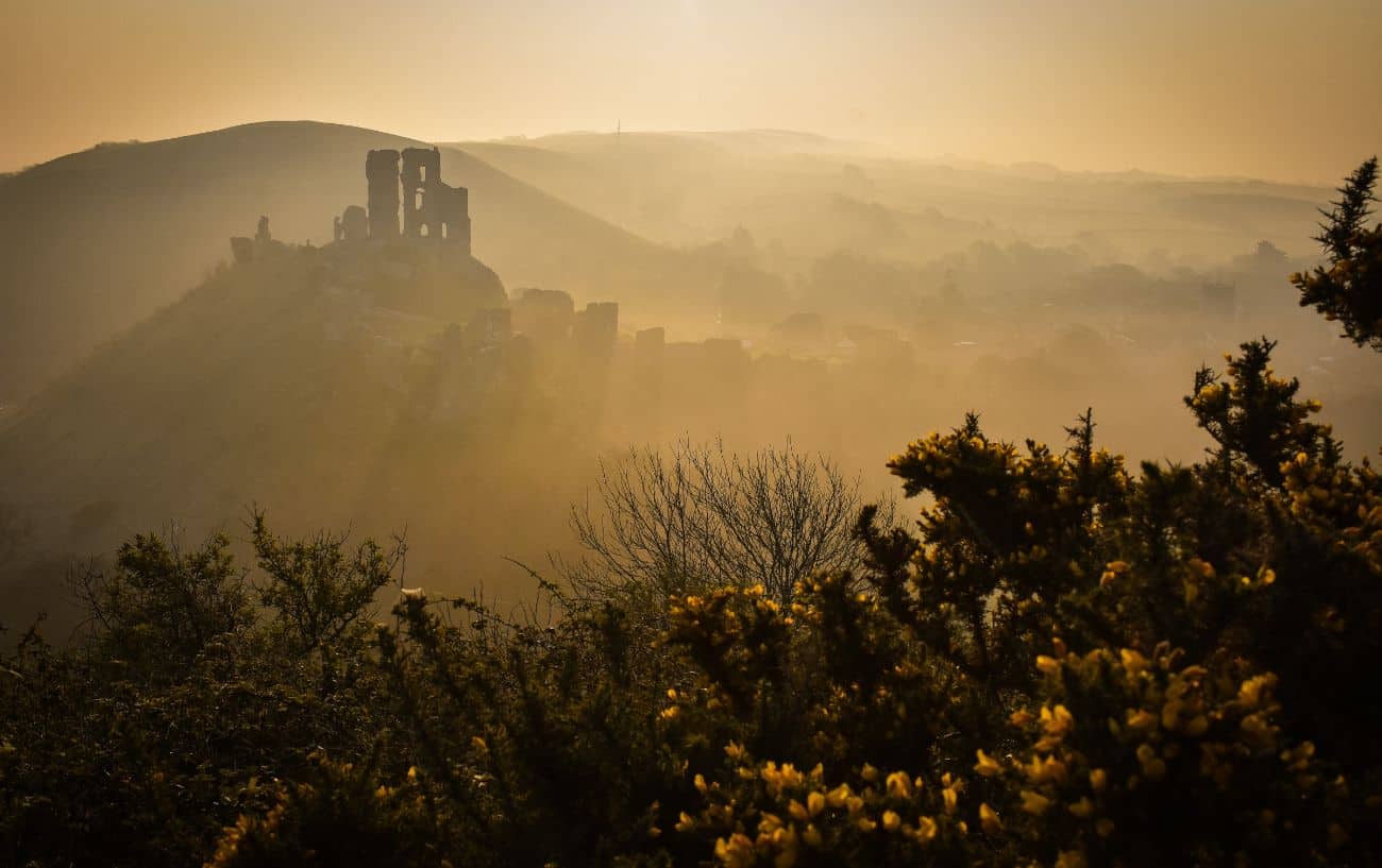 Sunrise view of the ruins of Corfe Castle and the valley beyond.