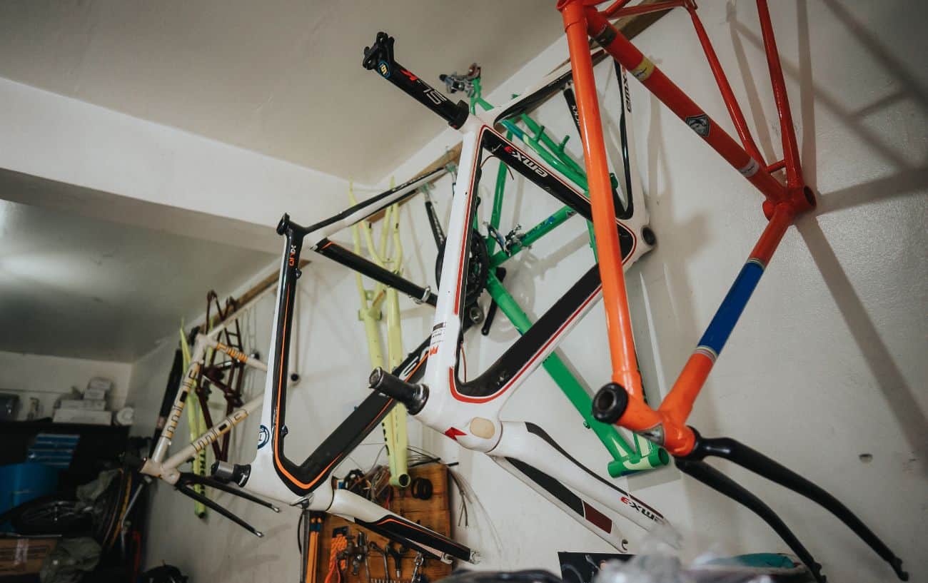 Four bike framesets hang on the wall of a garage.