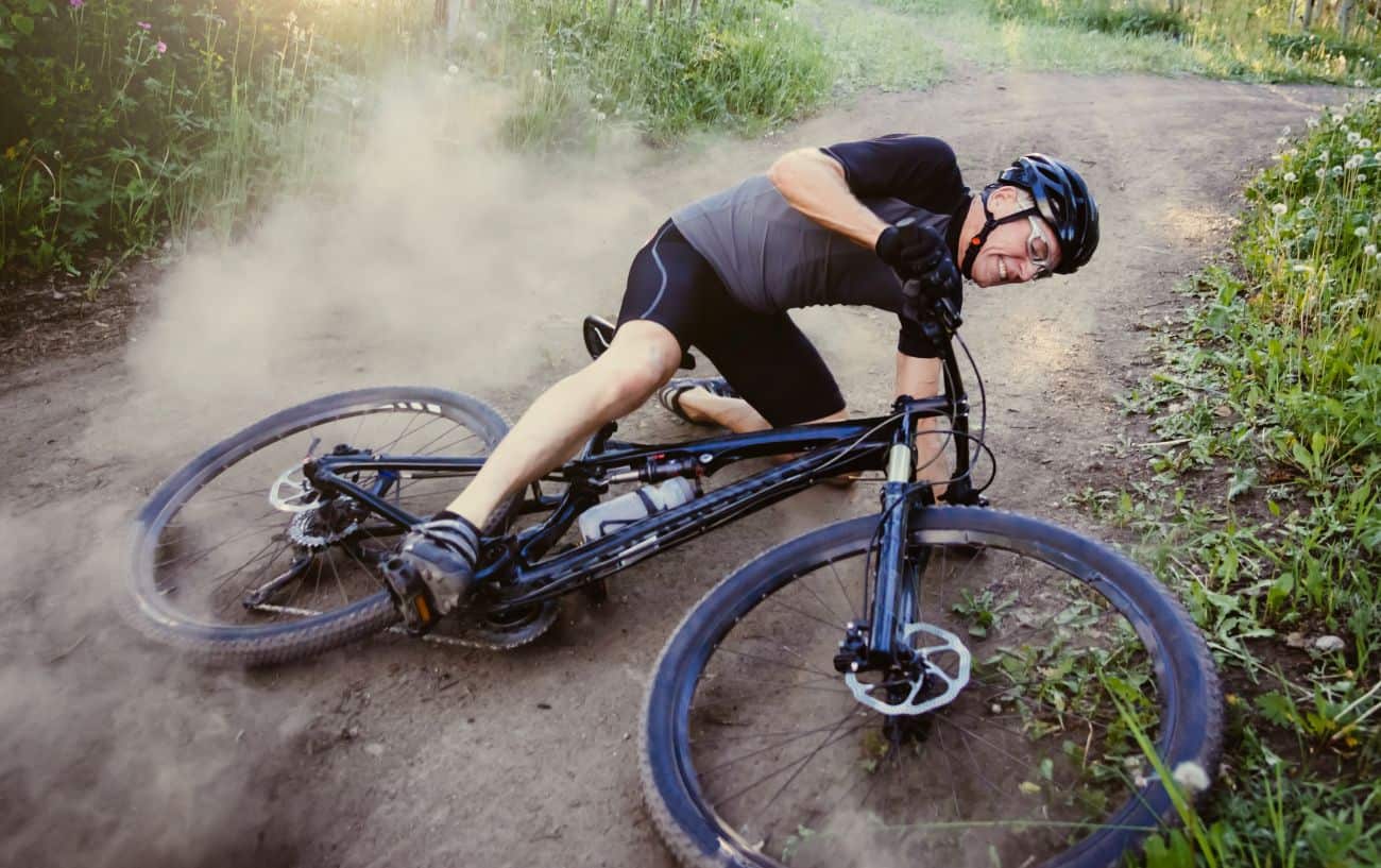 A cyclist takes a tumble off his black mountain bike.