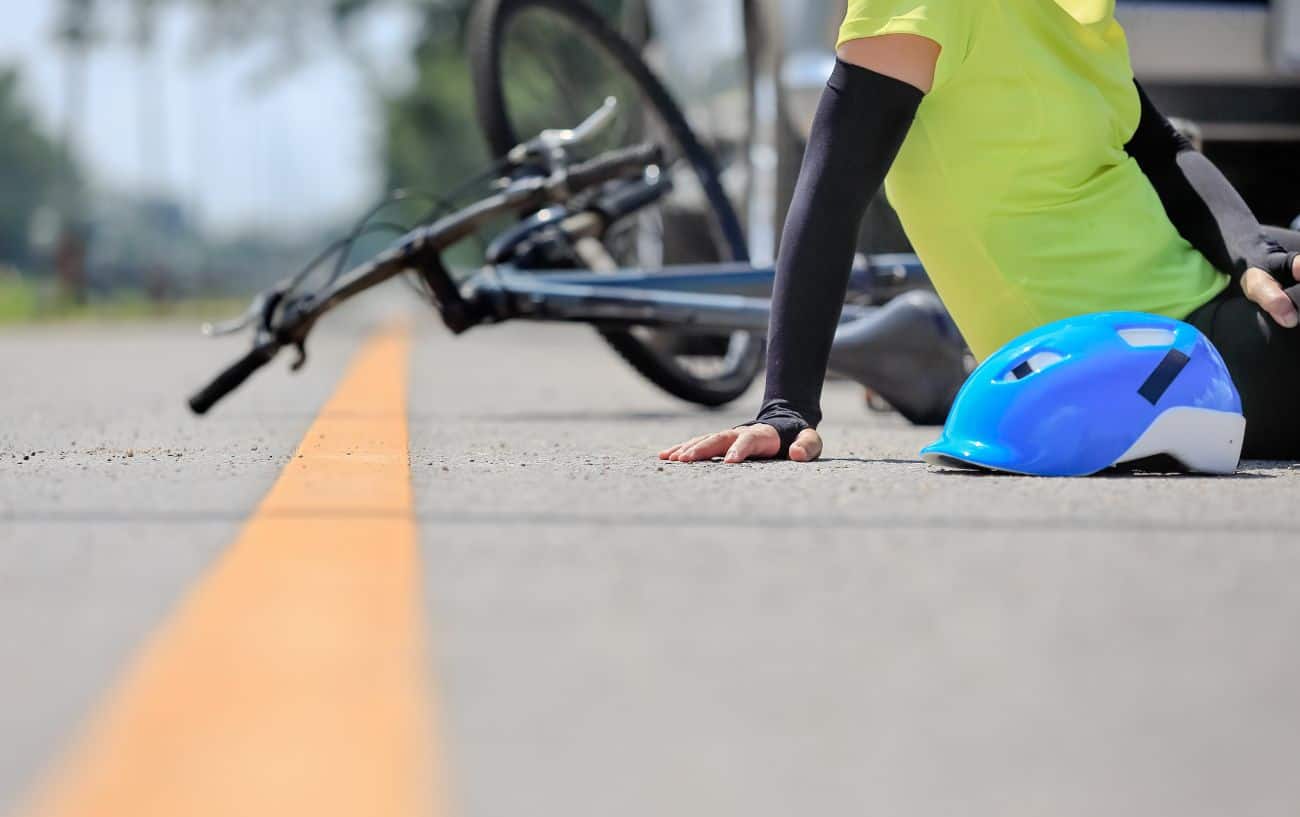 A cyclist sits on the road with road rash after a fall.