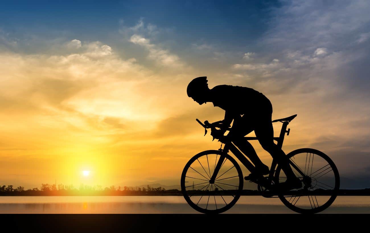 A cyclist sprints out of the saddle against a sunset backdrop.