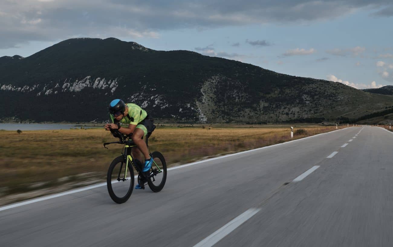 A cyclist on a triathlon bike sprints hard on a flat valley road.