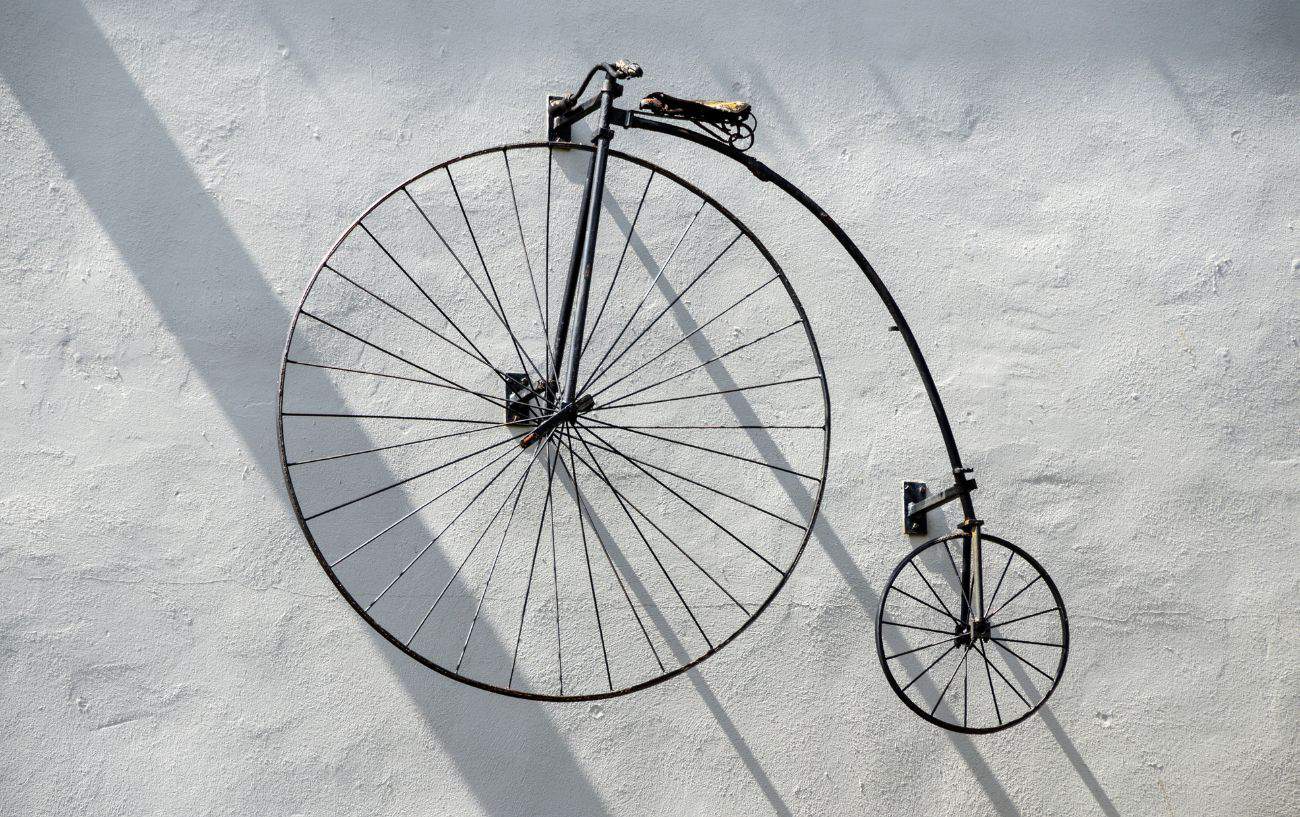 A black penny farthing bike hangs on a whitewashed wall.