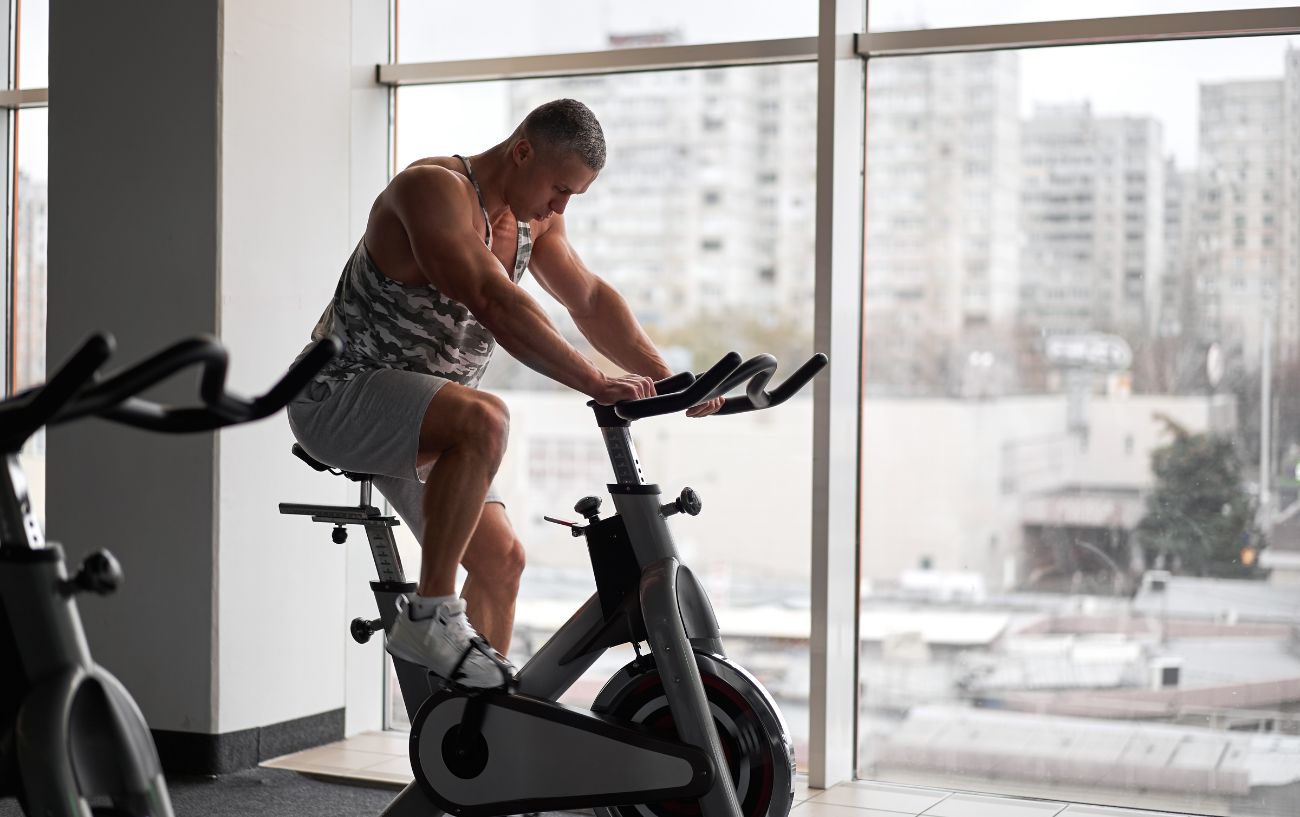 A man chases the stationary bike benefits in front of a window with a grey cityscape.