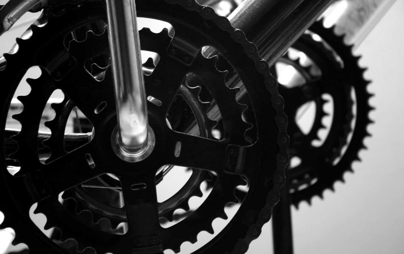 Black and white close-up of two triple chainsets on road bikes.