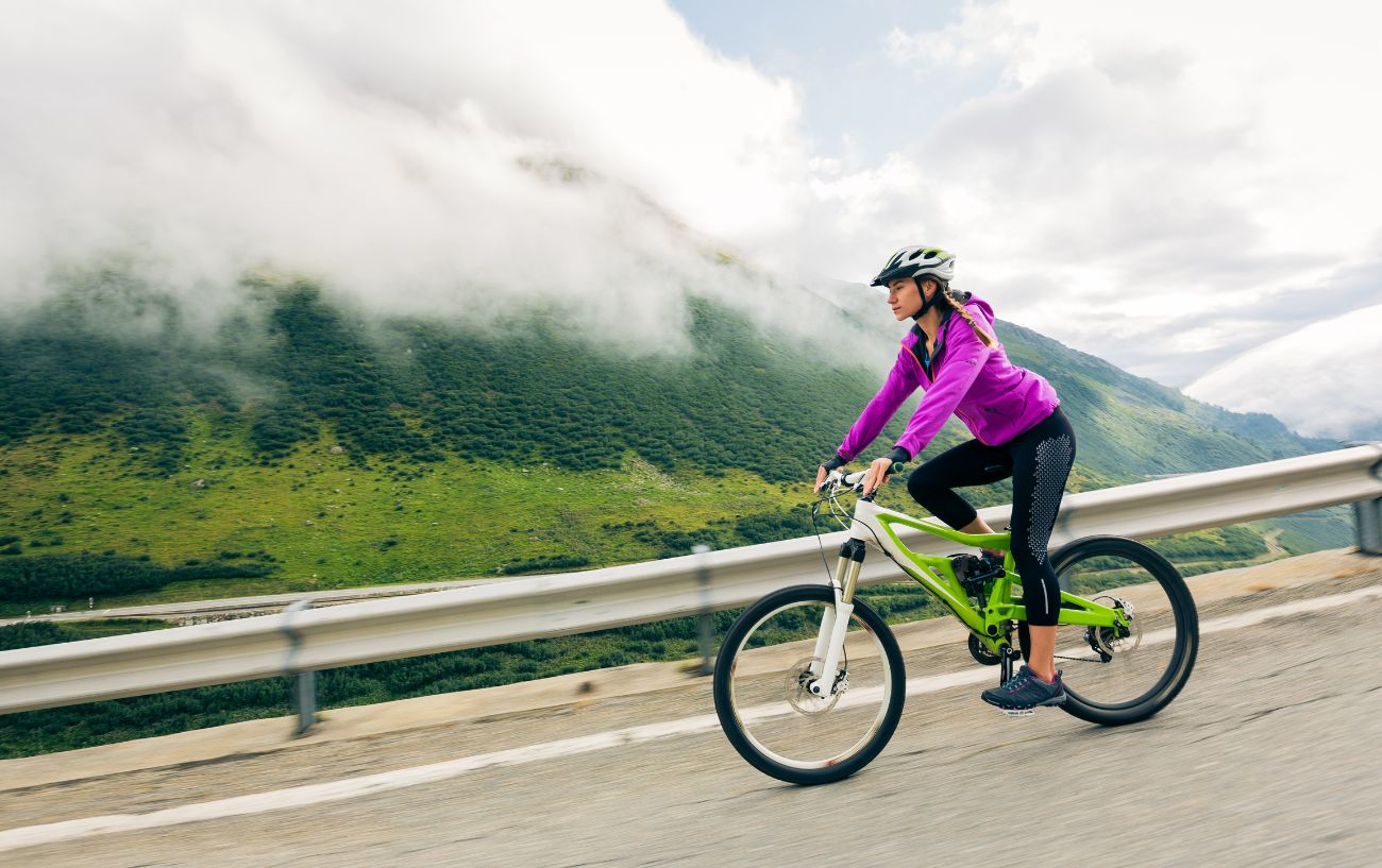 A cyclist in a pink jacket descends a mountainous road.
