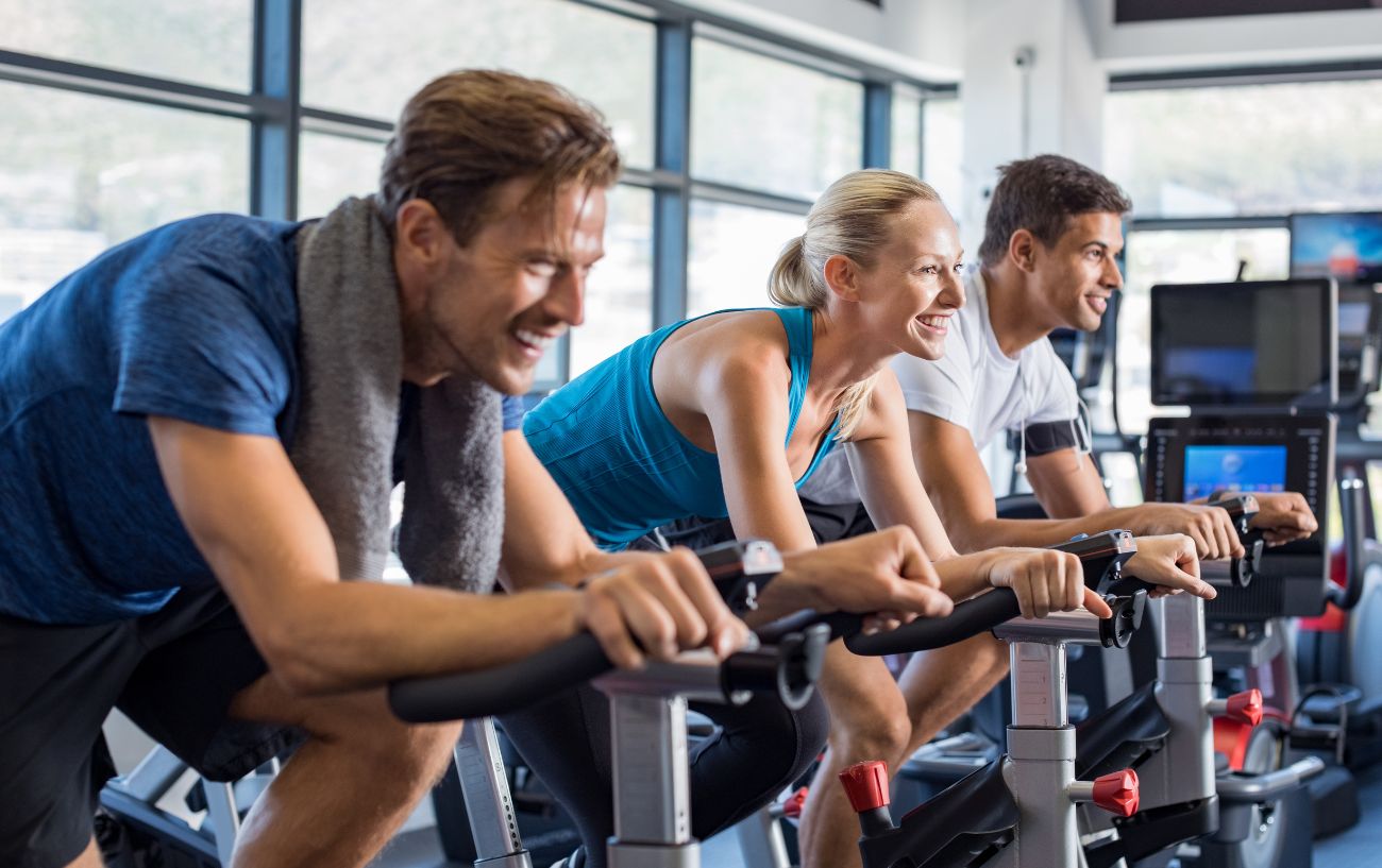 Three cyclists ride spin bikes at the gym.