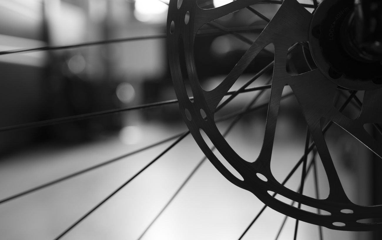 Black and white photo of a road bike disc brake with a soft-focus city in the background.