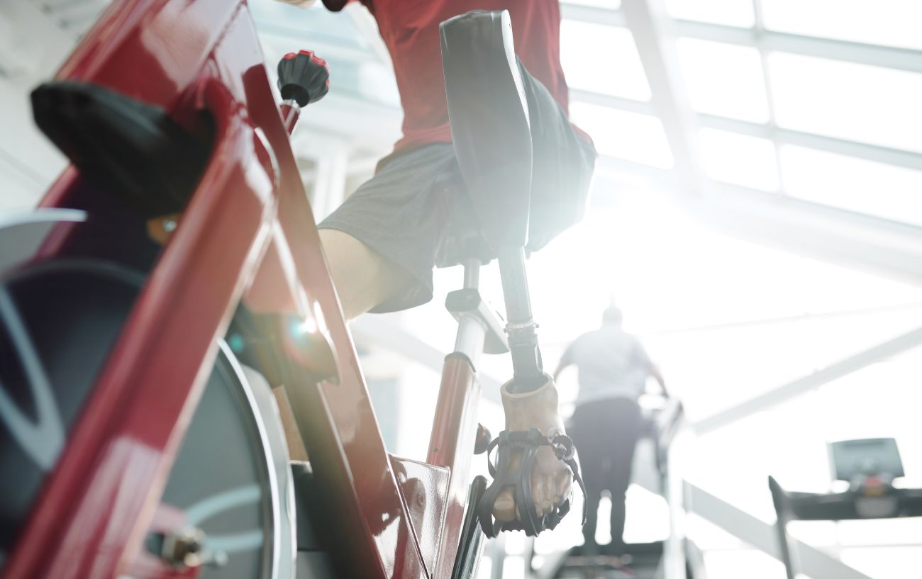 A cyclist with a prosthetic leg rides a red stationary bike in a gym.