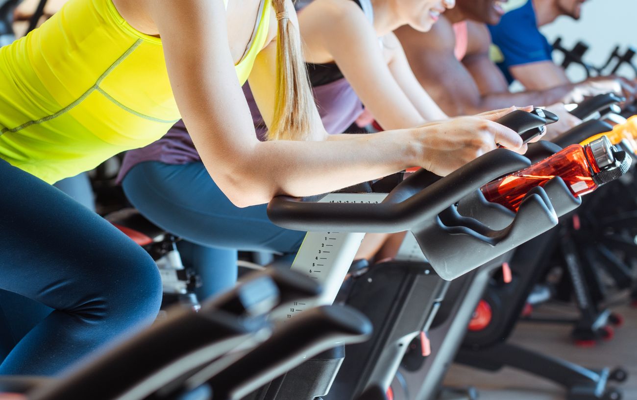 Four cyclists ride stationary bikes in a gym.