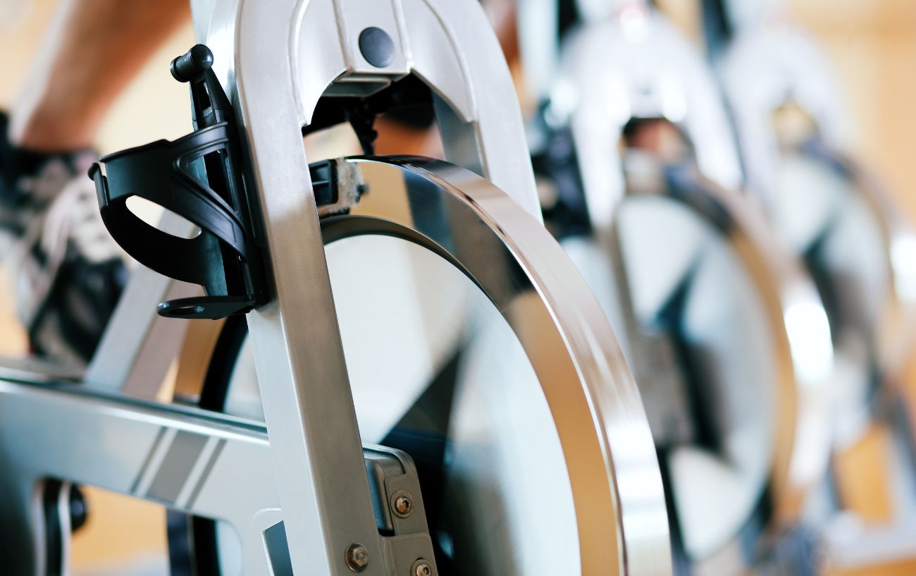 A row of silver spin bikes lined up next to each other at a gym.